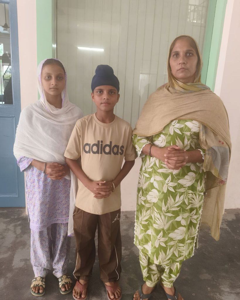 A woman standing with two children outside a building, the boy wearing a patka.