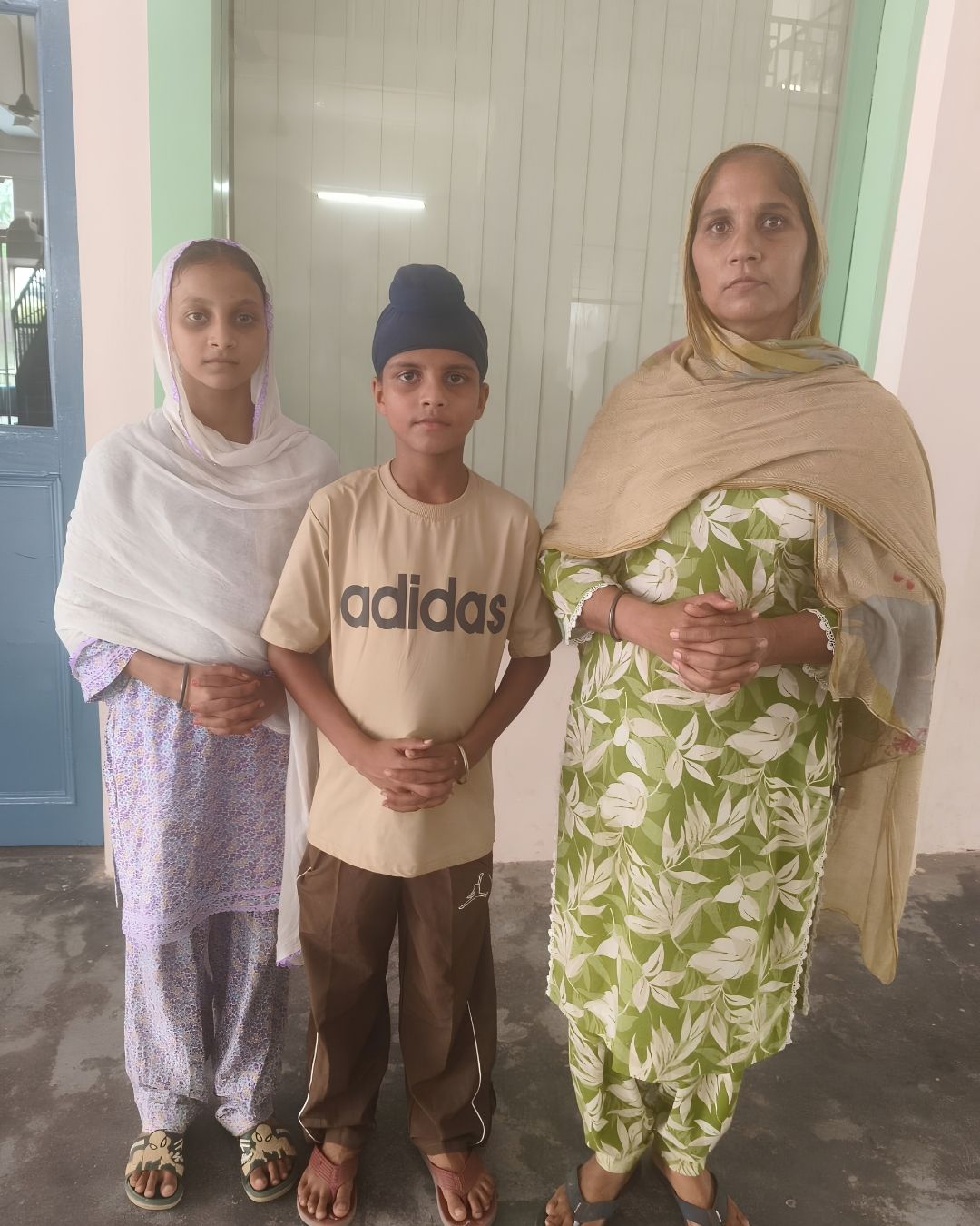 A woman standing with two children outside a building, the boy wearing a patka.