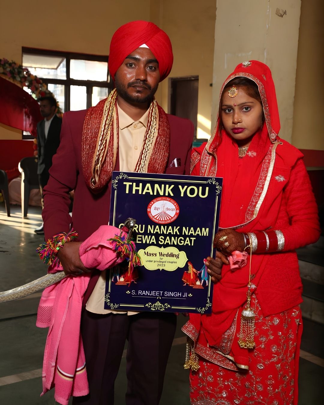 A newly married couple holding a card thanking Guru Nanak Naam Leva Sangat for the mass wedding held for underprivileged couples.